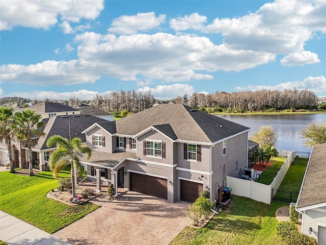 traditional-style house featuring stucco siding, a water view, fence, a garage, and a front lawn