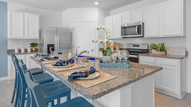 kitchen with stone countertops, appliances with stainless steel finishes, a breakfast bar, white cabinetry, and a sink