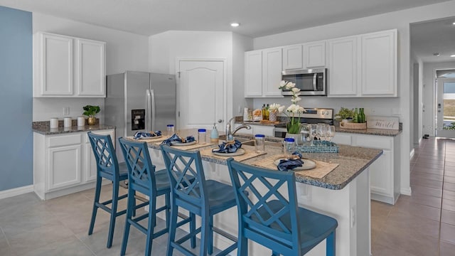 kitchen with stainless steel appliances, white cabinetry, a sink, and a breakfast bar area