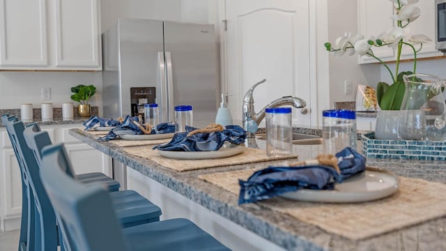 kitchen with a sink, stainless steel fridge, white cabinetry, and a kitchen breakfast bar