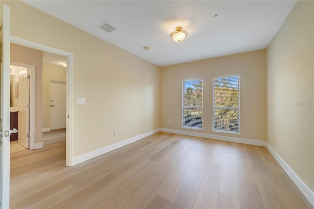 spare room with light wood-type flooring, visible vents, and baseboards