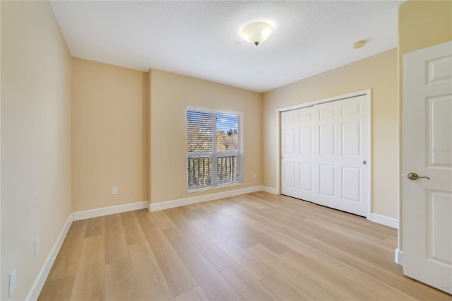 unfurnished bedroom with light wood-style floors, a textured ceiling, baseboards, and a closet