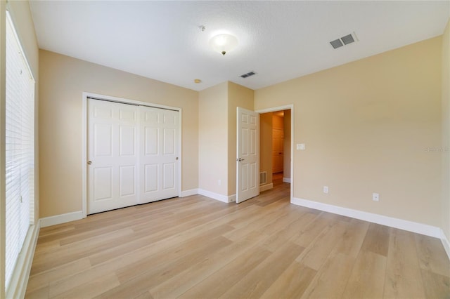 unfurnished bedroom featuring light wood finished floors, baseboards, visible vents, and a closet