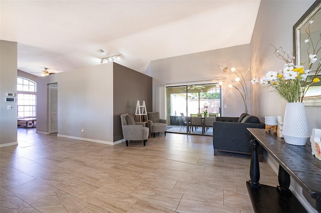 interior space featuring a ceiling fan, lofted ceiling, a healthy amount of sunlight, and baseboards