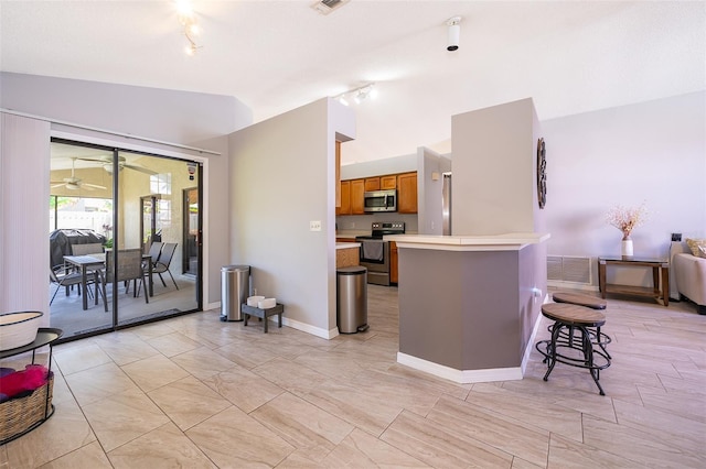 kitchen with appliances with stainless steel finishes, brown cabinets, a breakfast bar area, a peninsula, and vaulted ceiling