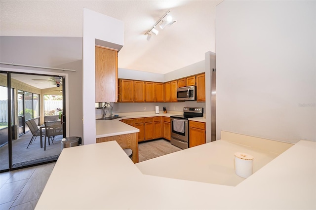 kitchen with stainless steel appliances, a sink, light countertops, brown cabinetry, and track lighting