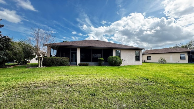 rear view of house with a sunroom, a lawn, and stucco siding