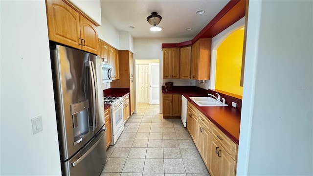 kitchen with light tile patterned floors, appliances with stainless steel finishes, dark countertops, and a sink