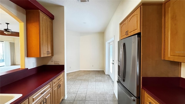 kitchen with stainless steel fridge, baseboards, a ceiling fan, dark countertops, and light tile patterned flooring