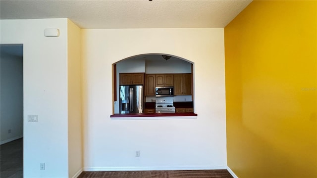 kitchen with a textured ceiling, stainless steel appliances, dark countertops, and baseboards