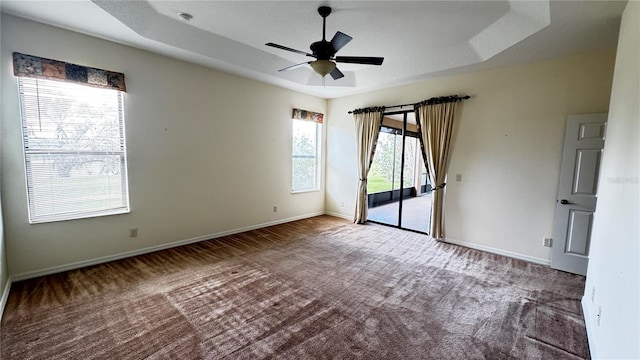 carpeted empty room with baseboards, a raised ceiling, and a ceiling fan