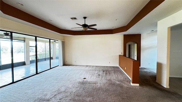 carpeted empty room featuring ceiling fan, visible vents, a tray ceiling, and baseboards