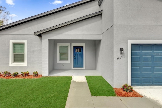 view of exterior entry with a garage, a yard, and stucco siding