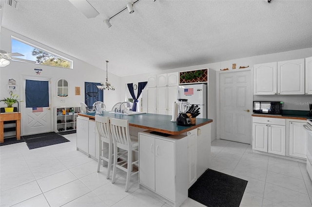 kitchen featuring black microwave, vaulted ceiling, dark countertops, and freestanding refrigerator