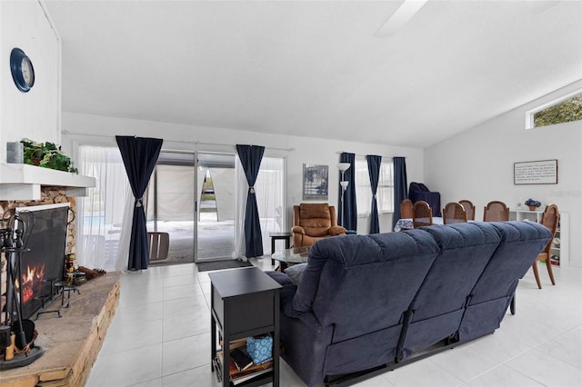 living area with a wealth of natural light, vaulted ceiling, a stone fireplace, and light tile patterned floors