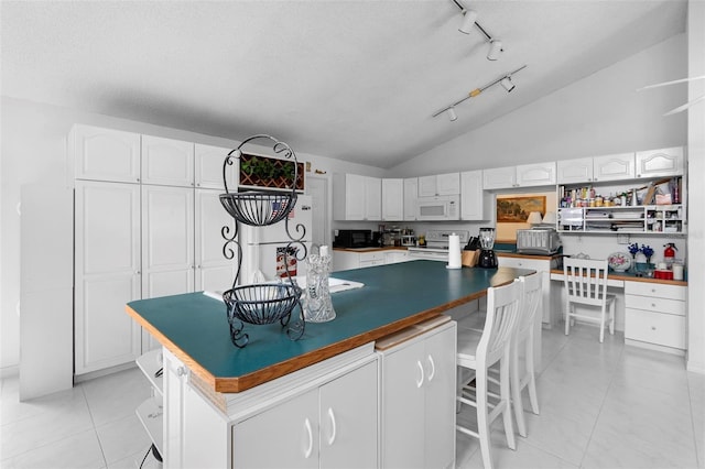 kitchen featuring lofted ceiling, light tile patterned floors, white appliances, a breakfast bar, and white cabinetry