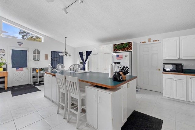 kitchen featuring black microwave, lofted ceiling, white cabinets, freestanding refrigerator, and dark countertops