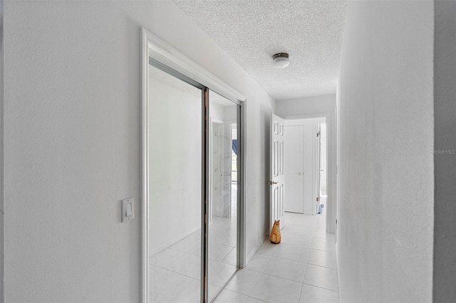 hall featuring a textured wall, a textured ceiling, and light tile patterned flooring