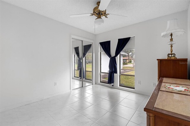 unfurnished room featuring a ceiling fan, a textured ceiling, baseboards, and light tile patterned floors