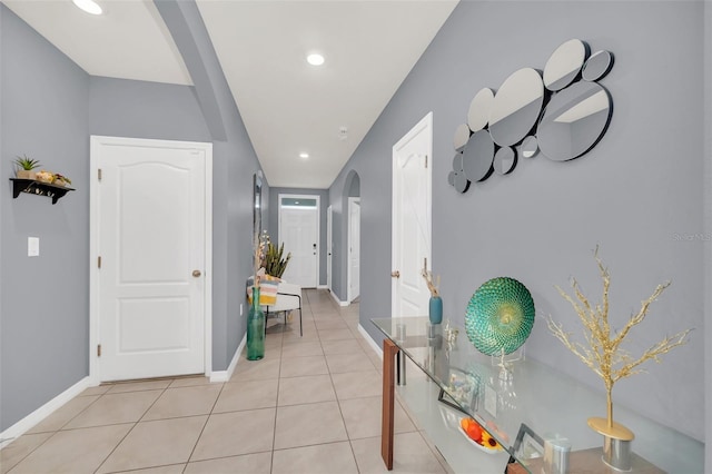 corridor featuring arched walkways, recessed lighting, baseboards, and light tile patterned floors