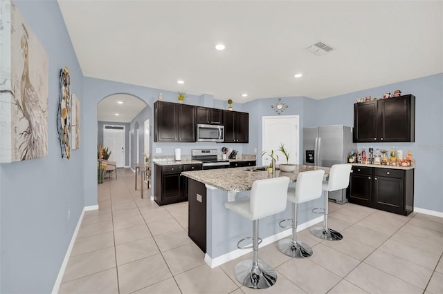 kitchen with arched walkways, a breakfast bar, stainless steel appliances, visible vents, and a sink