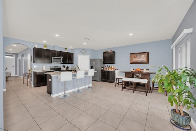 kitchen featuring arched walkways, a breakfast bar area, appliances with stainless steel finishes, a kitchen island with sink, and light countertops