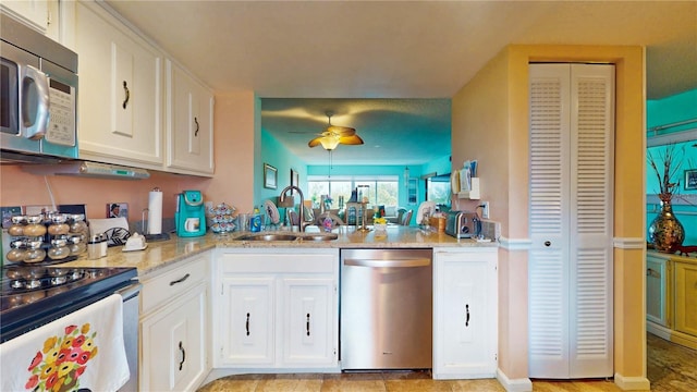 kitchen featuring stainless steel appliances, a ceiling fan, white cabinets, a sink, and light stone countertops