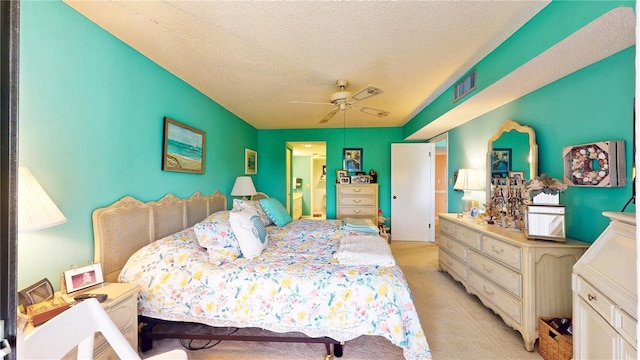 bedroom featuring a textured ceiling, ensuite bathroom, light colored carpet, a ceiling fan, and visible vents