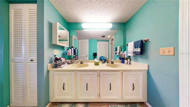 bathroom with double vanity, a sink, a closet, and a textured ceiling