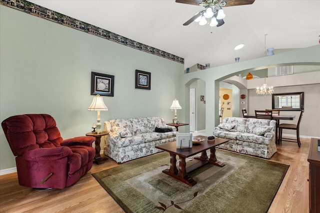 living area with ceiling fan with notable chandelier, arched walkways, baseboards, and wood finished floors