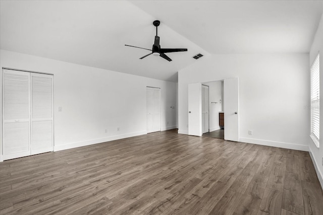 unfurnished bedroom featuring wood finished floors, visible vents, baseboards, vaulted ceiling, and two closets