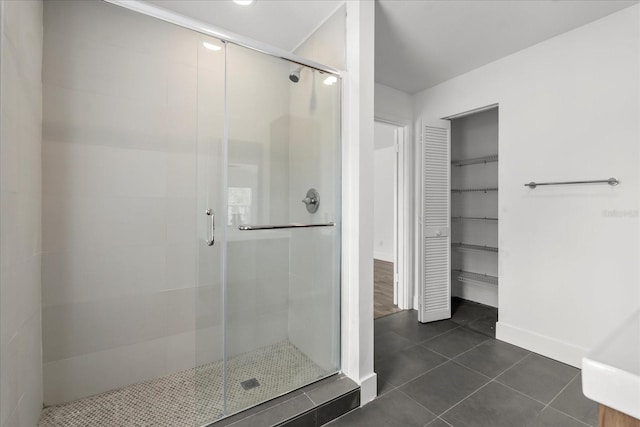 bathroom with a spacious closet, a stall shower, tile patterned flooring, and baseboards