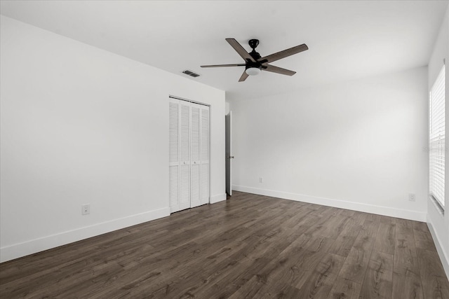 unfurnished bedroom featuring dark wood-style floors, a closet, visible vents, a ceiling fan, and baseboards