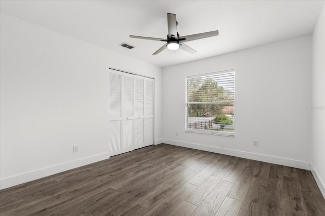 unfurnished bedroom featuring dark wood-type flooring, a closet, visible vents, and baseboards