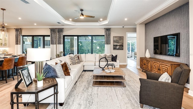 living area with ornamental molding, a tray ceiling, light wood-type flooring, and recessed lighting