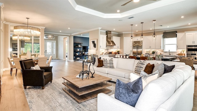 living room with ceiling fan with notable chandelier, light wood-style floors, recessed lighting, and crown molding