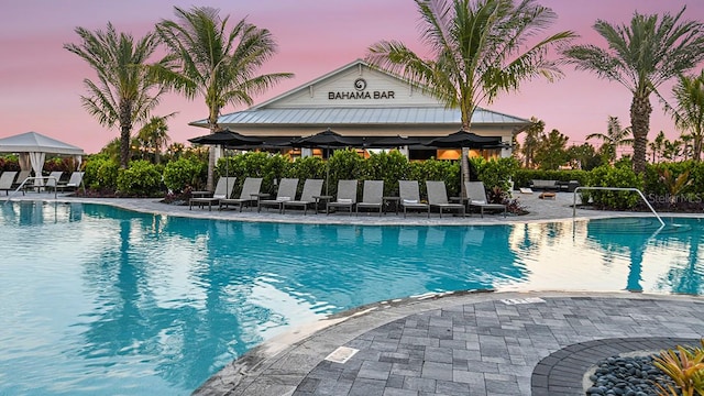 pool at dusk featuring a gazebo, a patio area, and a community pool