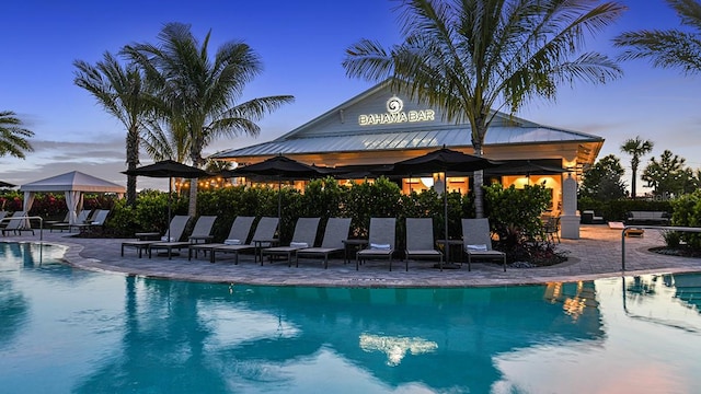 pool at dusk featuring a gazebo, a patio, and a community pool