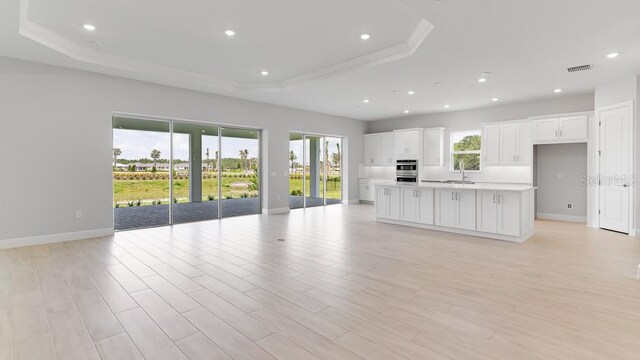 5641 Nevis Ter, Kissimmee, FL 34758 - unfurnished living room with a tray ceiling, a sink, baseboards, ornamental molding, and light wood-style floors