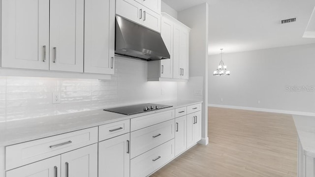 5641 Nevis Ter, Kissimmee, FL 34758 - kitchen with under cabinet range hood, black electric cooktop, backsplash, white cabinets, and light wood-style flooring