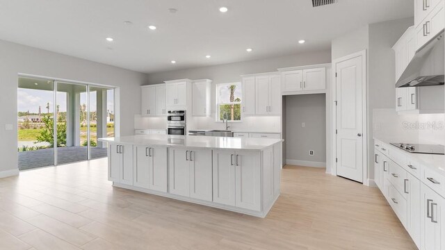 5641 Nevis Ter, Kissimmee, FL 34758 - kitchen with double oven, black electric stovetop, a center island, white cabinetry, and under cabinet range hood