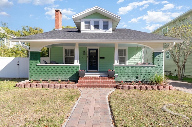 bungalow-style home with a gate, fence, roof with shingles, covered porch, and a front lawn