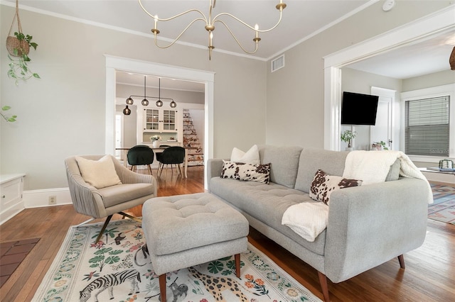 living area featuring a chandelier, visible vents, crown molding, and wood finished floors