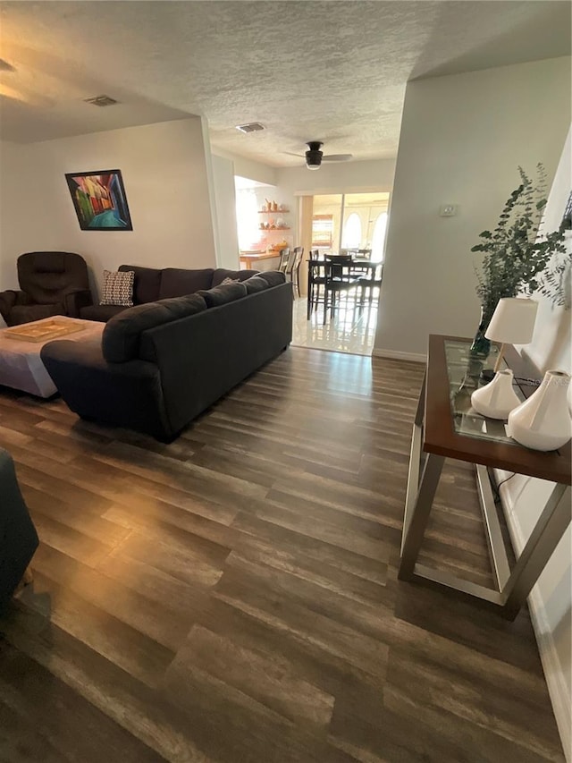 living room featuring a textured ceiling, ceiling fan, wood finished floors, visible vents, and baseboards