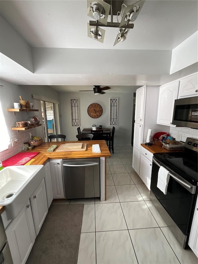 kitchen featuring a peninsula, appliances with stainless steel finishes, wood counters, and white cabinetry