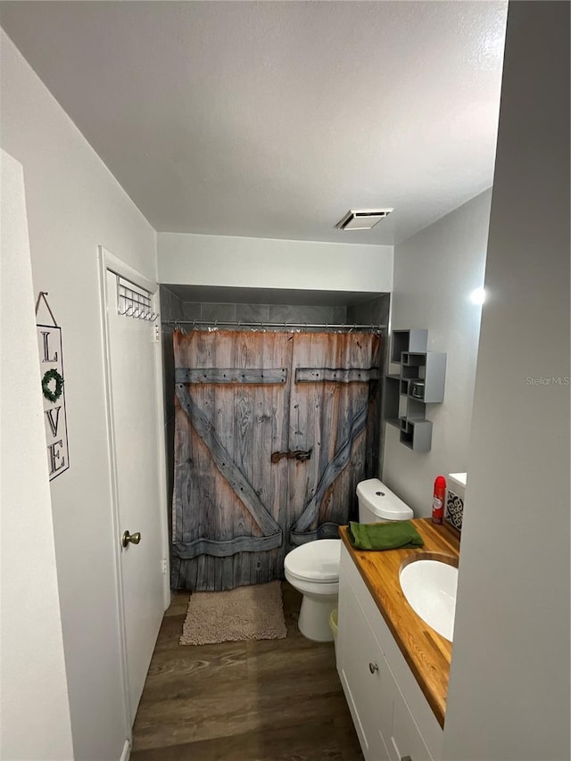 bathroom featuring curtained shower, toilet, wood finished floors, visible vents, and vanity