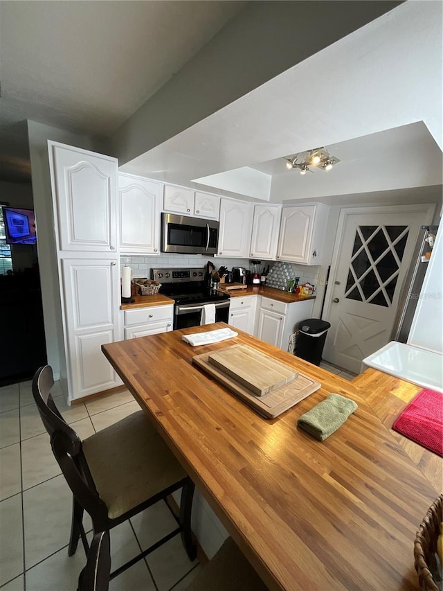 kitchen with light tile patterned floors, butcher block counters, decorative backsplash, appliances with stainless steel finishes, and white cabinets