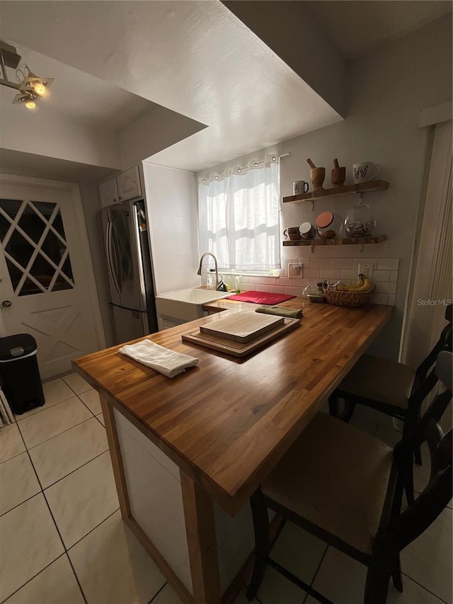 kitchen featuring butcher block countertops, light tile patterned flooring, backsplash, and freestanding refrigerator