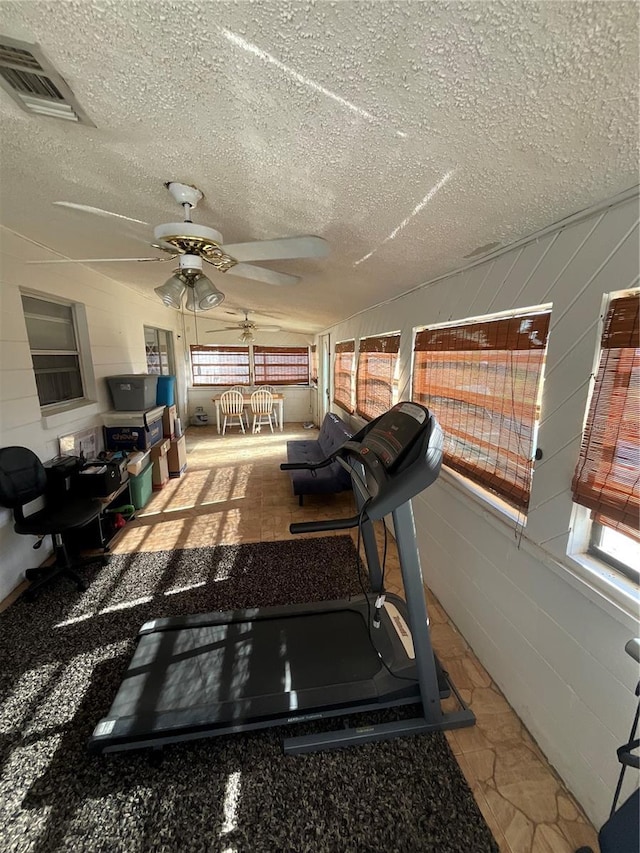 workout room featuring vaulted ceiling, a textured ceiling, visible vents, and a healthy amount of sunlight