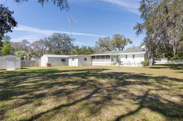 rear view of house featuring a storage shed, an outdoor structure, fence, a sunroom, and a yard